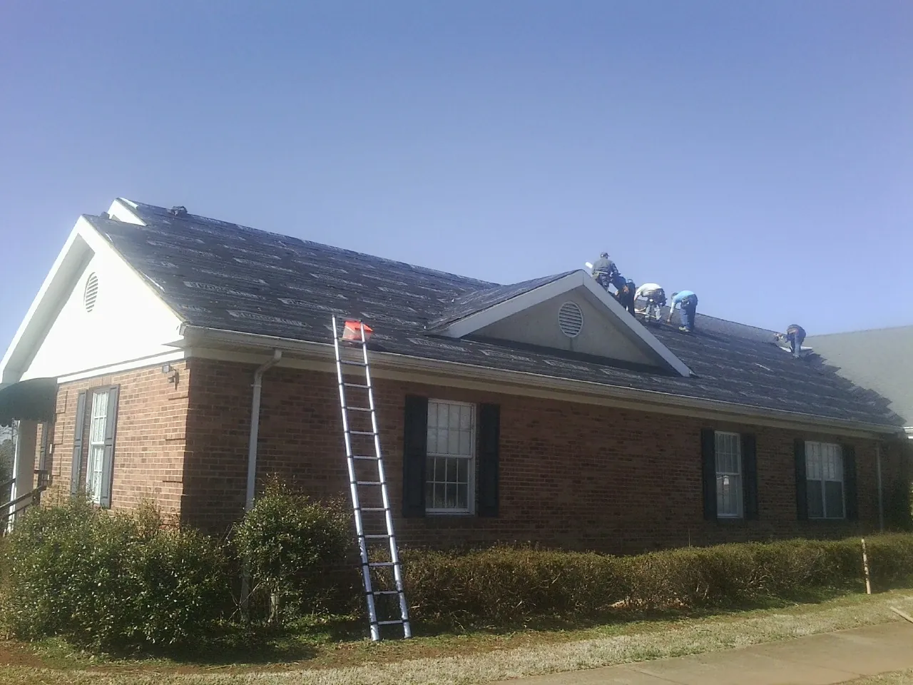 Crew tearing shingles off a brick ranch roof with a ladder set — Emergency Roof Repair work by our crew in Peterboro