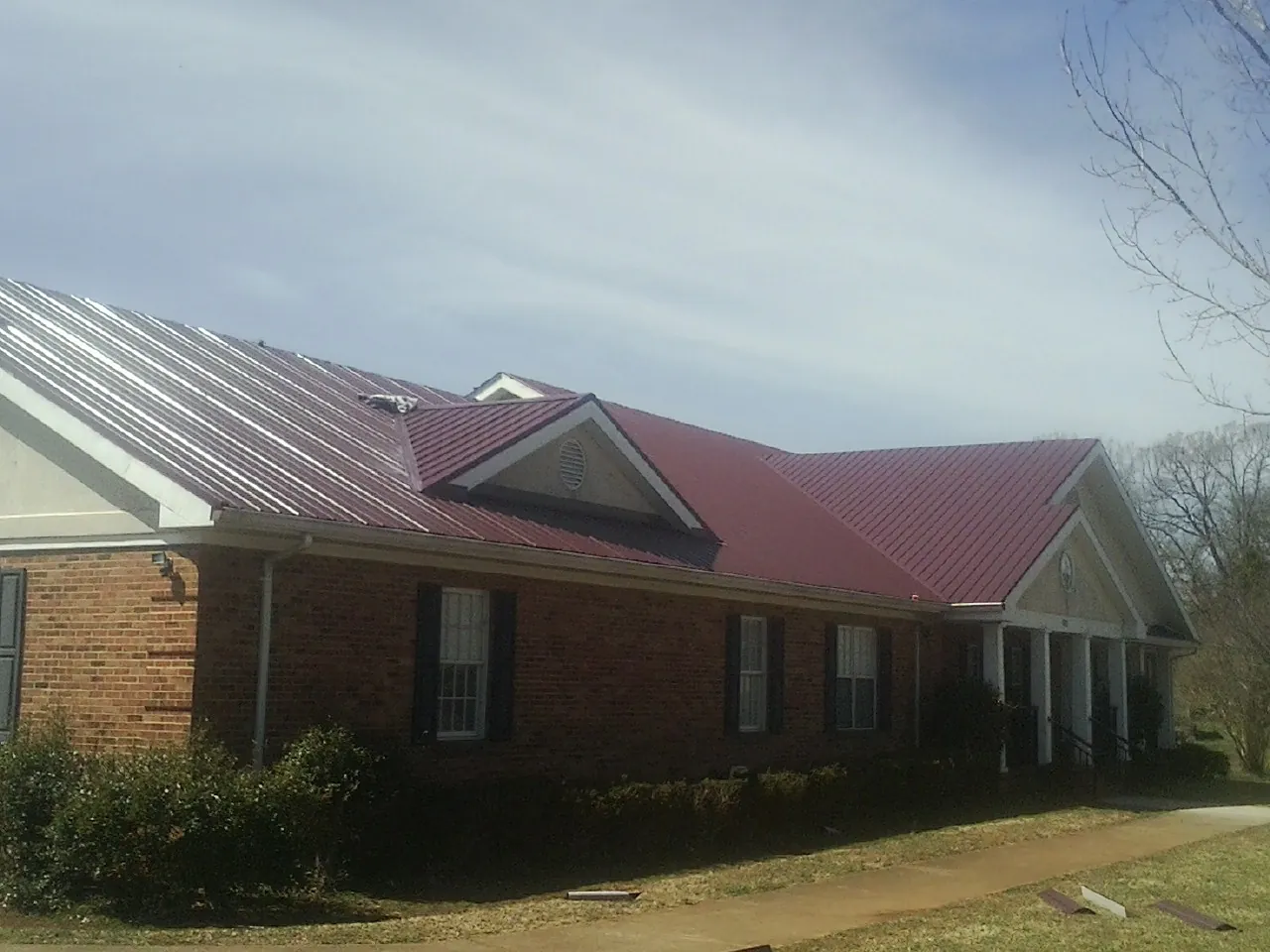Red metal roof with gabled entries on a long brick building, from a Hail Damage Roof Repair job in Peterboro