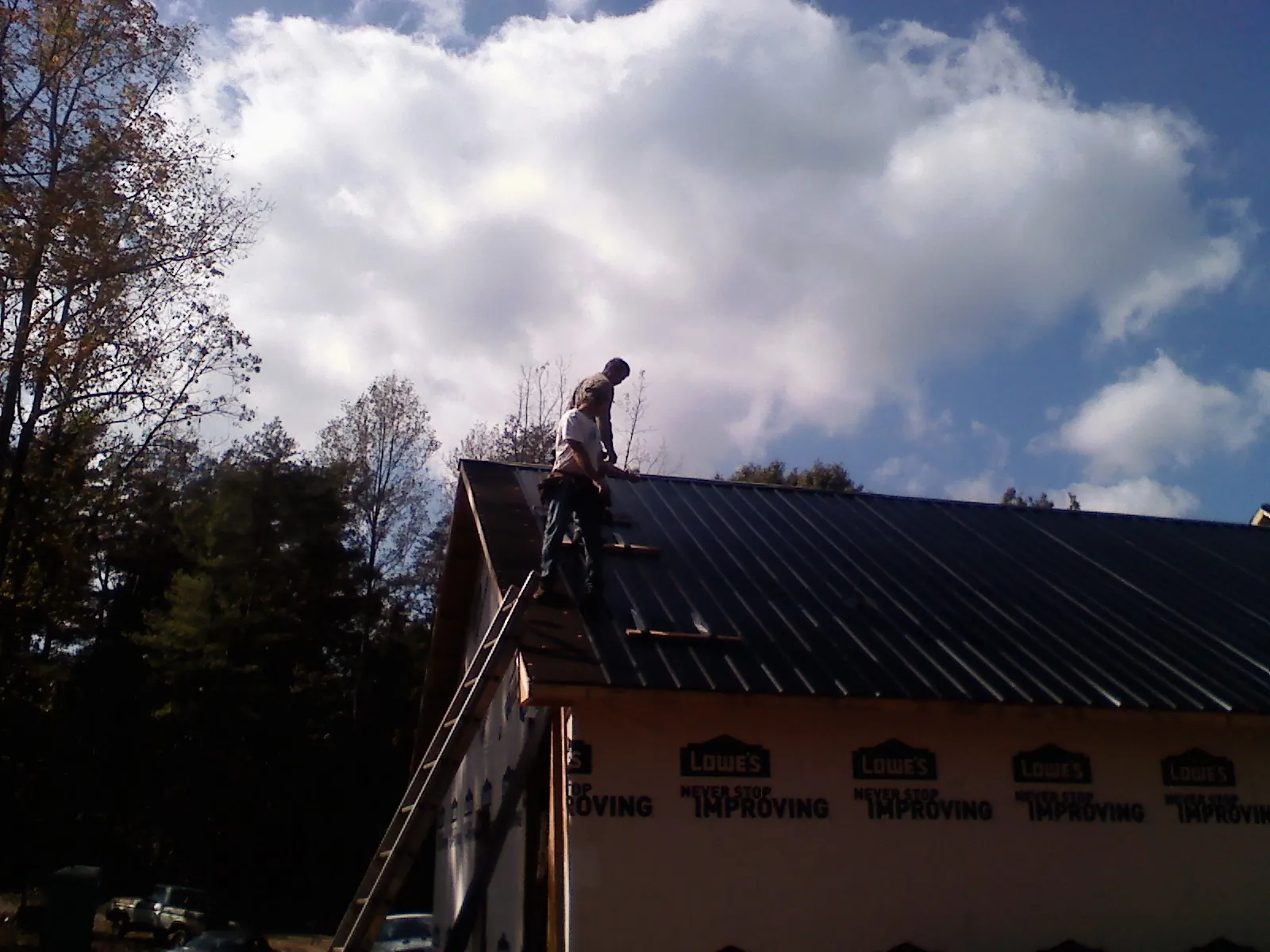 Roofer fastening dark metal panels high against a cloudy sky, from a Roof Inspection job in Peterboro