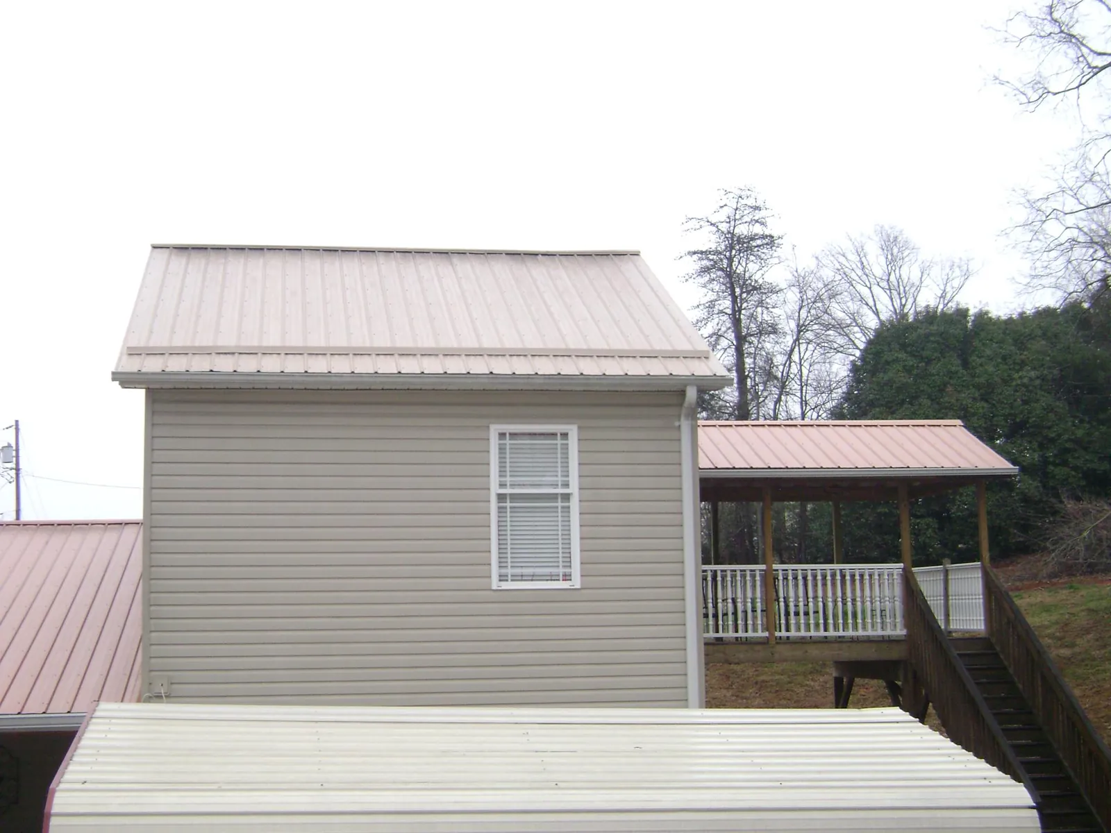 Tan metal roofs on a two story addition and attached porch, from a Roof Replacement job in Peterboro